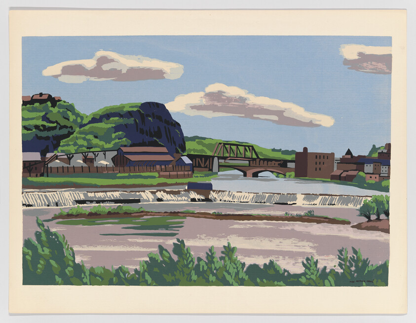 River with a cascading weir in front of a small town and a green steel bridge.