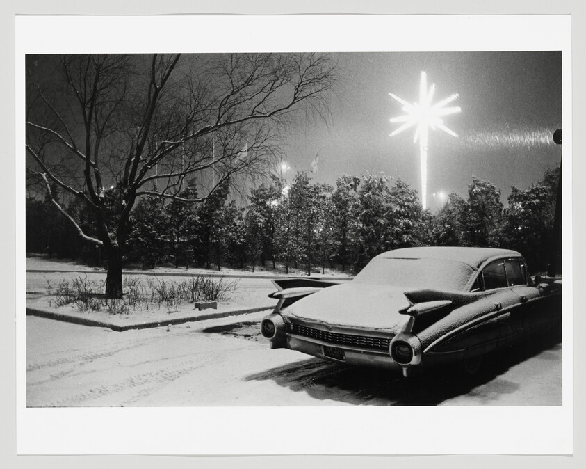 A snow-covered vintage car parked at night under a glowing star-shaped streetlight.