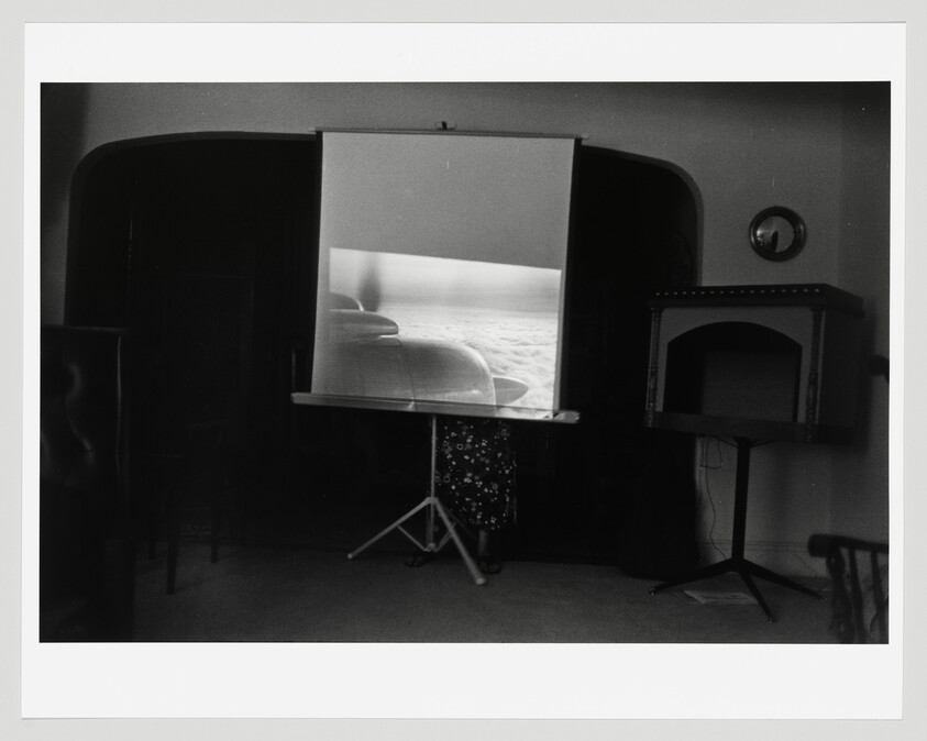 A projection screen shows an airplane engine view while a small tripod projector stands in a dim room.