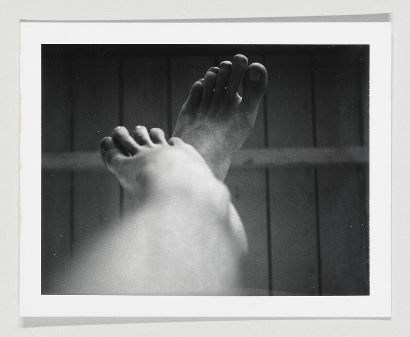 Bare feet raised and crossed against a wooden ceiling in a black-and-white photograph.