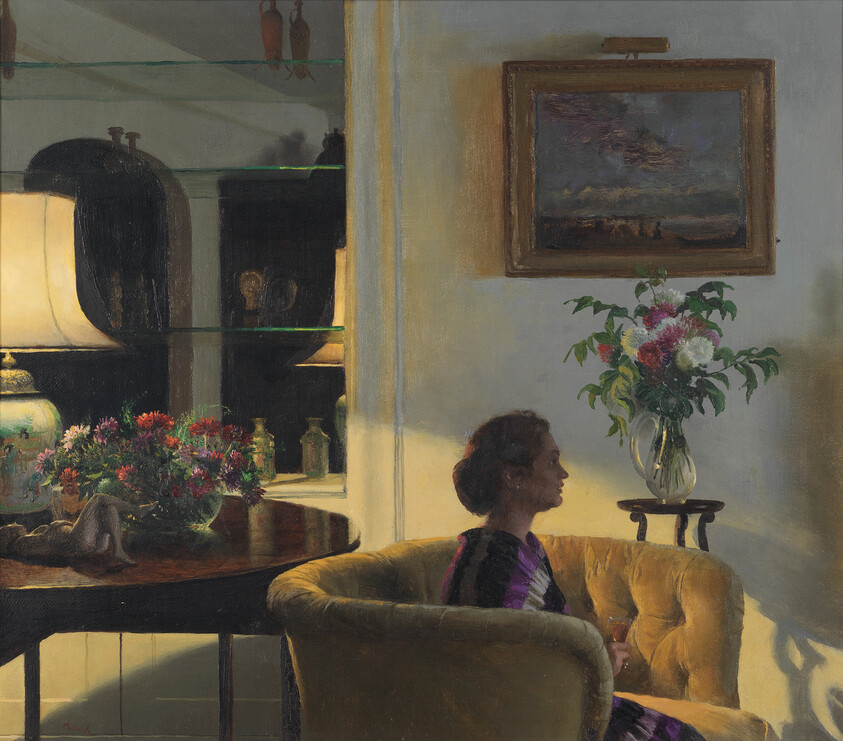 A woman sits on a yellow sofa in a softly lit room holding a glass.