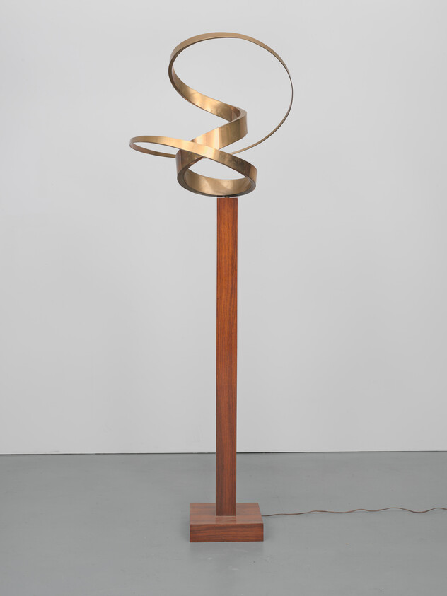 Tall floor lamp with a wooden base and a looping brass ribbon light at the top.