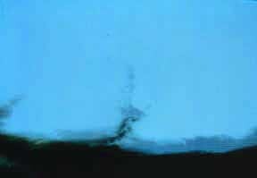 A thin twisted plume rises from a dark horizon against a bright blue background.