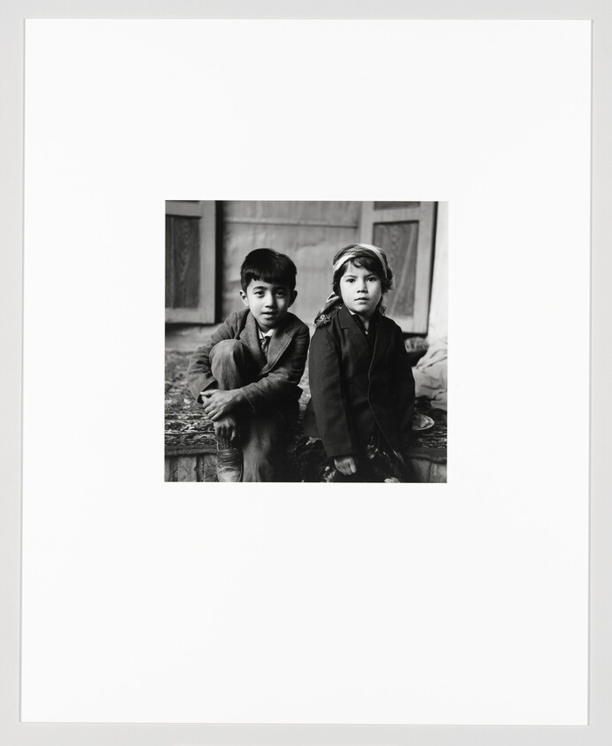 Two children sit side by side on a step, looking directly at the camera.