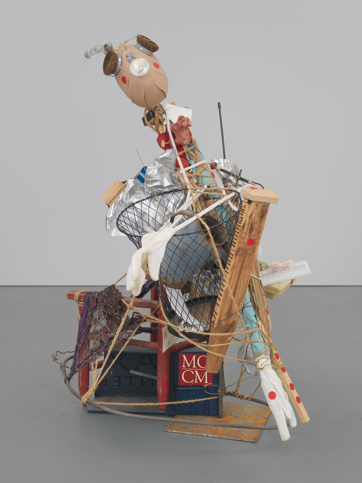 A tall assemblage sculpture made from household objects and string tied into a chaotic stack.