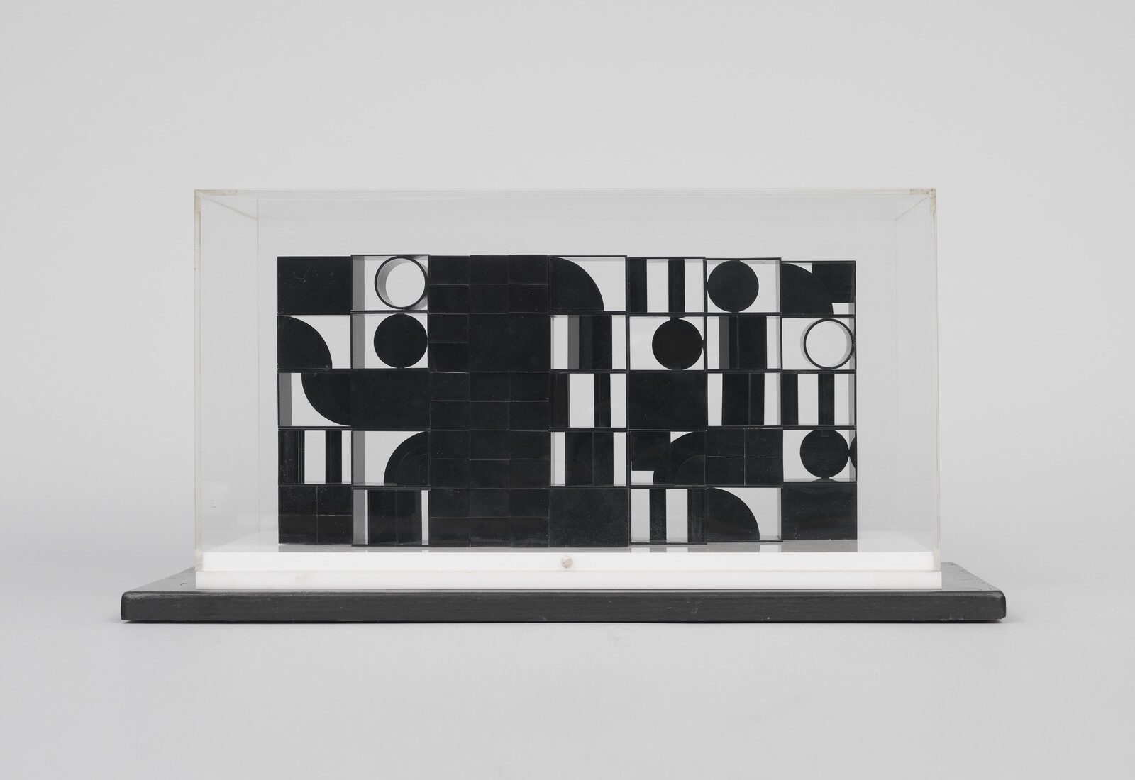 A rectangular glass case holds a black-and-white geometric tile arrangement on a white base.