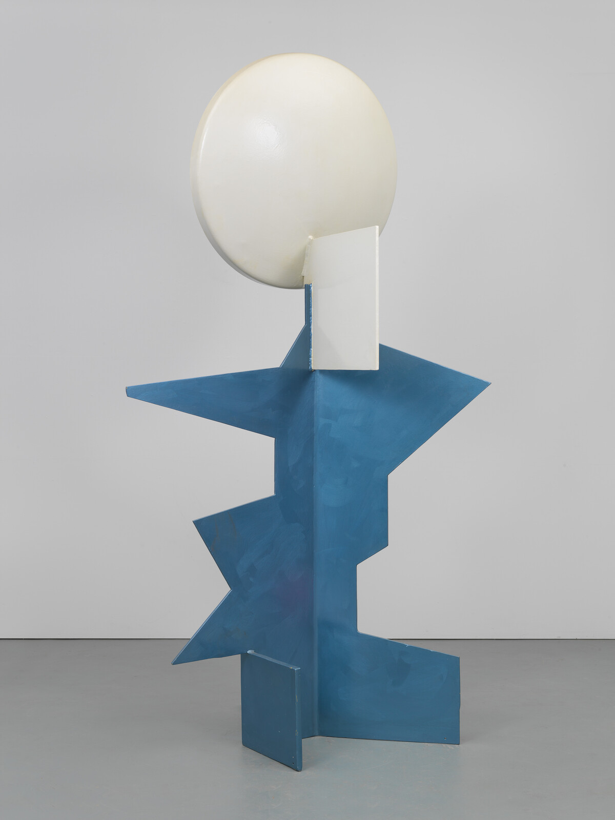 Tall blue angular metal sculpture supports a large white circular disk near the top.