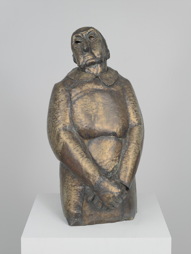 Bronze sculpture of a standing figure with folded hands and a tilted, contemplative head.