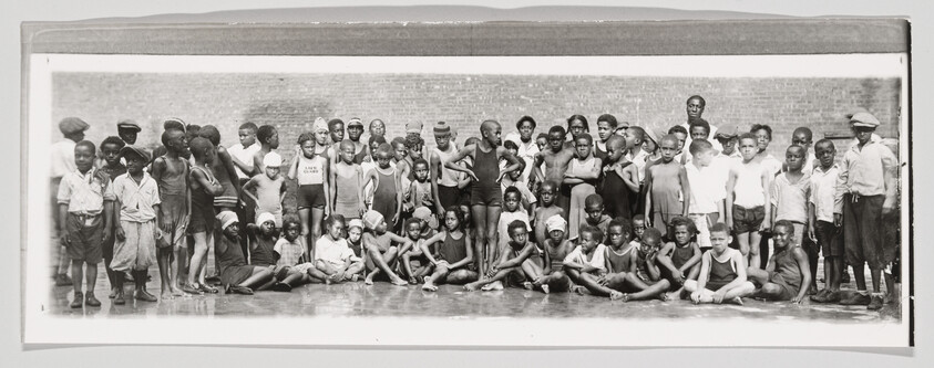 A large group of children in swimsuits and summer clothes gathered and posing on a wet courtyard.