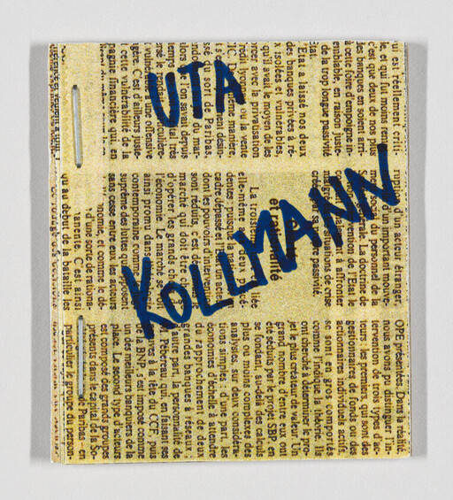 Blue handwritten text "KOLIMANN" across a square piece of newspaper with staples.