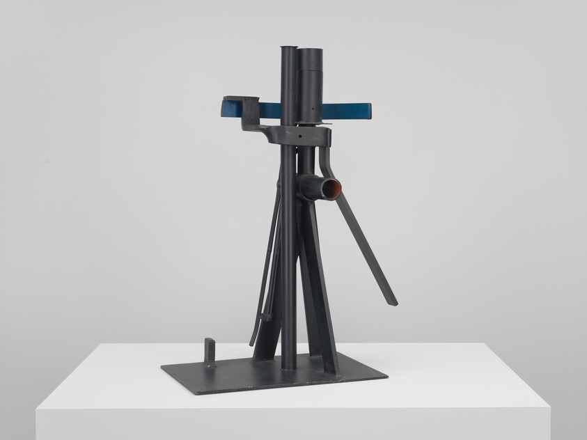 Black metal abstract sculpture with vertical rods and a blue crossbar on a white pedestal.