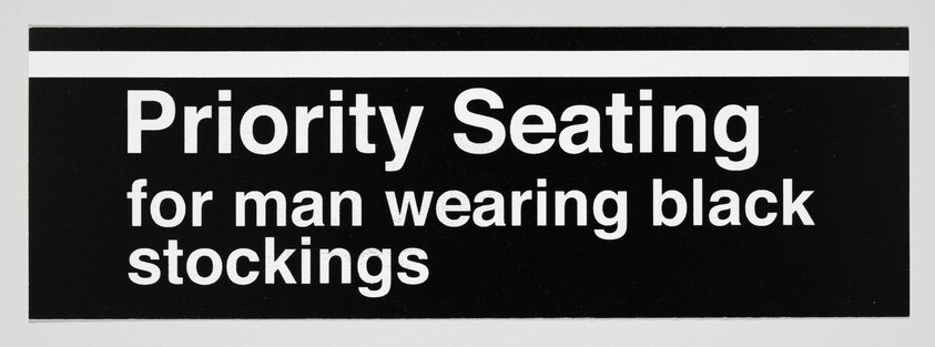 A rectangular sign with a black background and white text that reads "Priority Seating for man wearing black stockings."