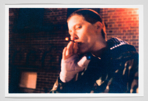 Young person smoking a cigarette outside at night against a brick wall.