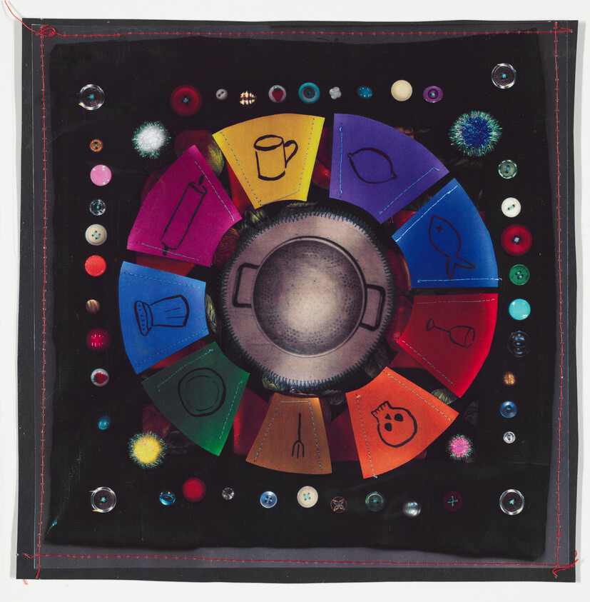 A colorful, circular board game with various symbols drawn on colored segments, surrounded by an assortment of buttons and beads on a black background. The central piece appears to be a metallic, pan-like object with two handles.