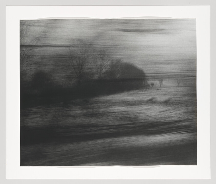 Blurred black-and-white landscape showing trees and fields streaked by horizontal motion.
