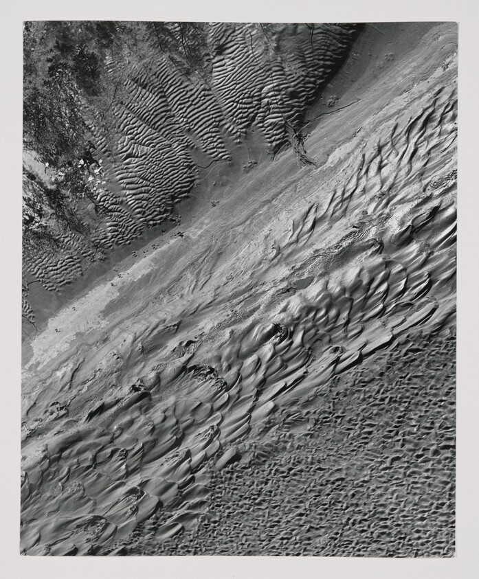 Wind-sculpted sand dunes and rippled desert surface seen from above.