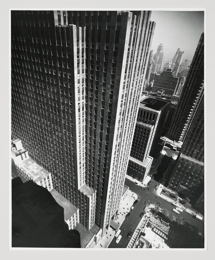 Tall Art Deco skyscraper towers over a busy city street with cars and pedestrians below.