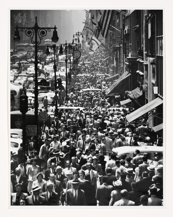 A densely packed mid-20th-century city sidewalk filled with pedestrians and vintage cars.