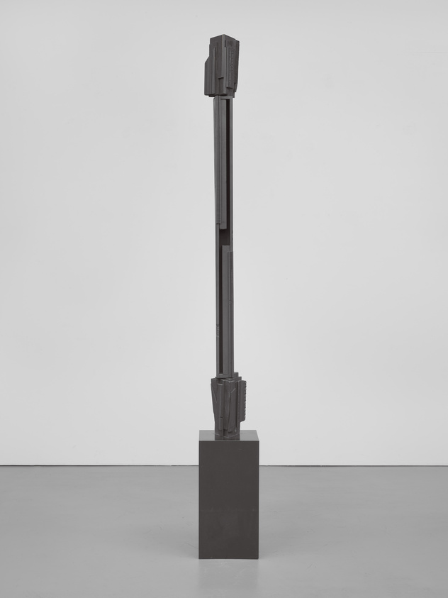 Tall, abstract metal sculpture on a dark pedestal, set against a plain white background.