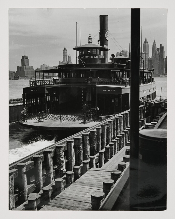 A steam ferry named Plainfield pulls into a wooden dock with city skyline beyond.