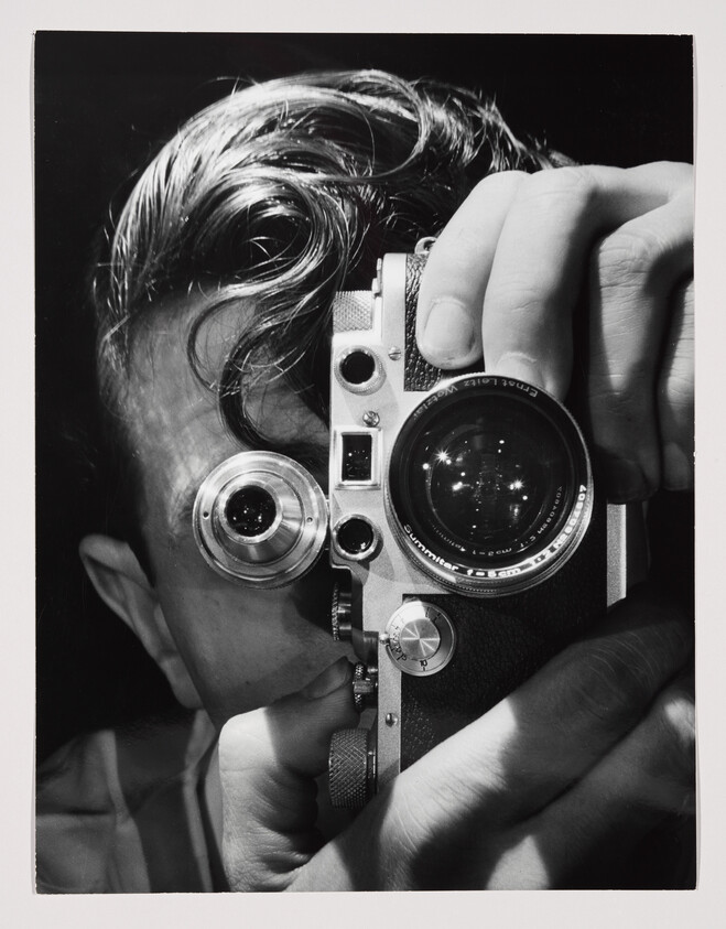 A person holds a vintage rangefinder camera up to their eye, preparing to take a photograph.