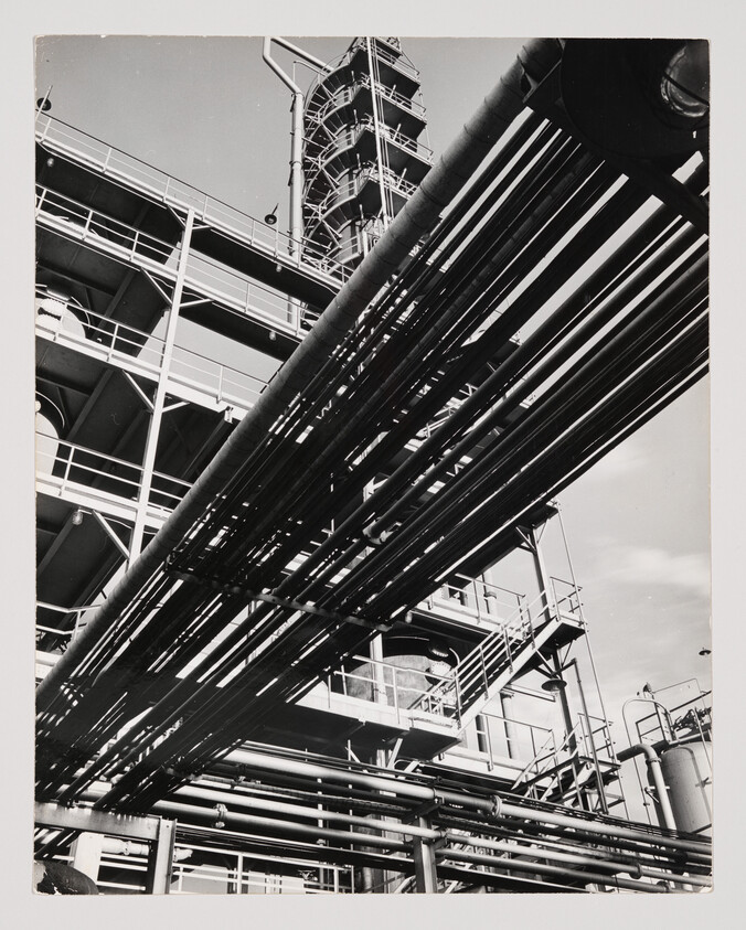 Multiple large industrial pipes run overhead across a steel plant structure with ladders and platforms.