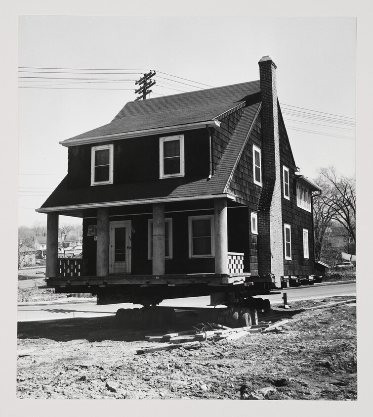 A two-story house is raised and transported on a flatbed trailer during relocation.