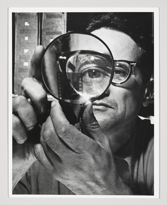Man inspects a strip of film through a magnifying glass, eye enlarged behind lens.