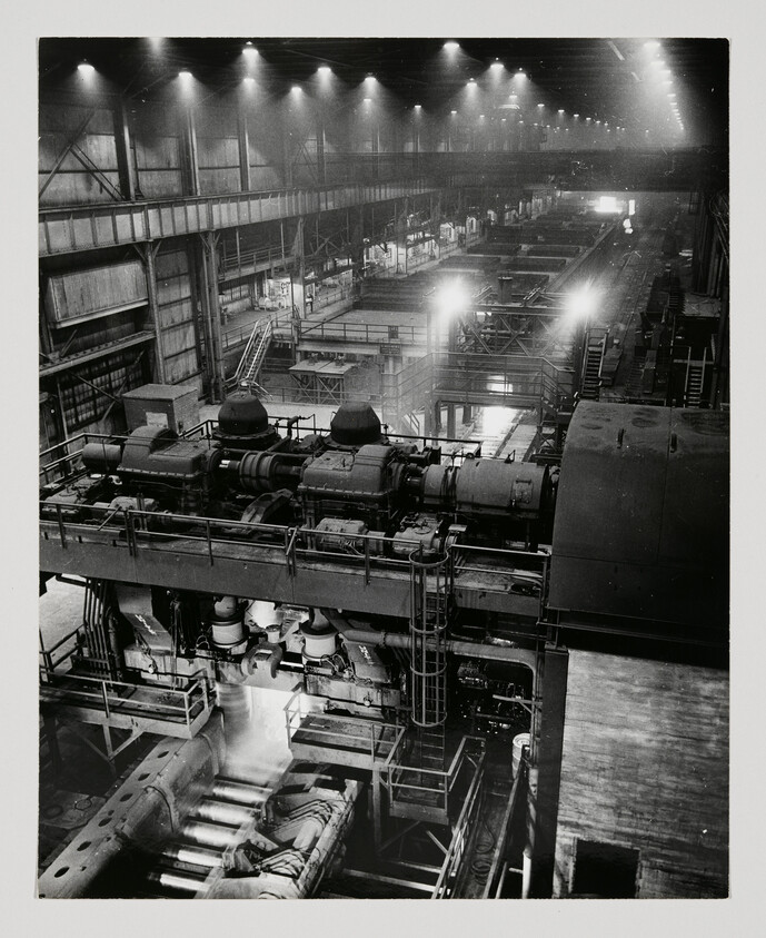 Massive factory hall with large industrial machines and glowing lights along the production line.