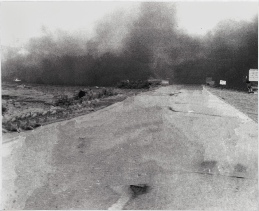 A cracked road leads toward a large dark smoke cloud blocking the horizon.