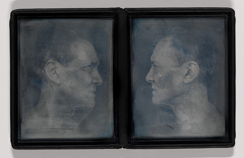 Two faded male profile portraits facing each other inside a small hinged display case.