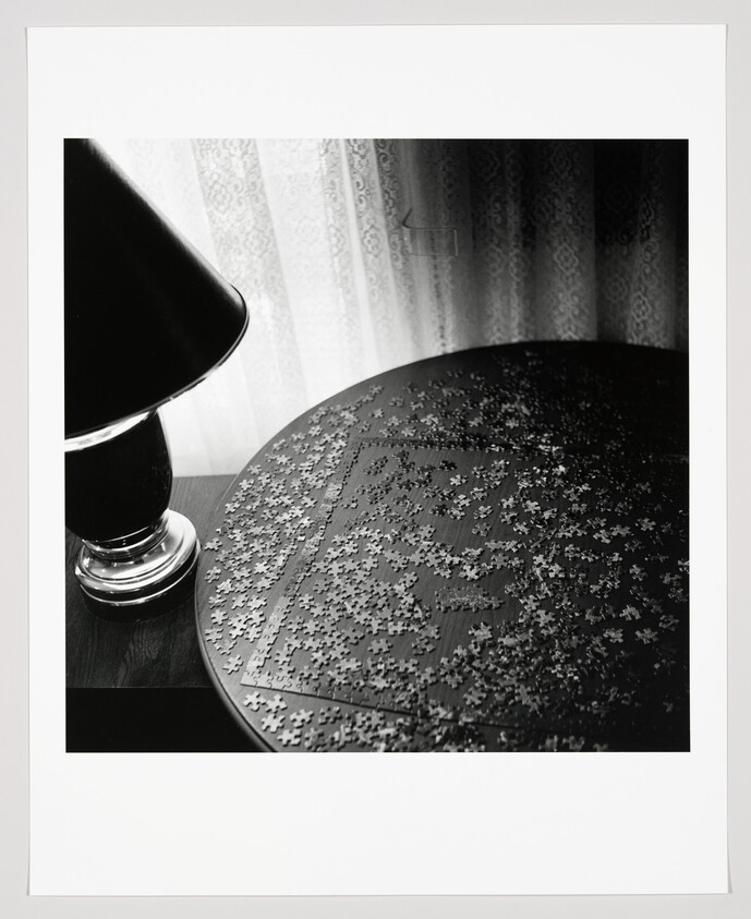 Round table covered with scattered jigsaw puzzle pieces beside a lit table lamp.