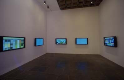 A dim gallery room with five wall-mounted flat screens displaying abstract blue and green images.