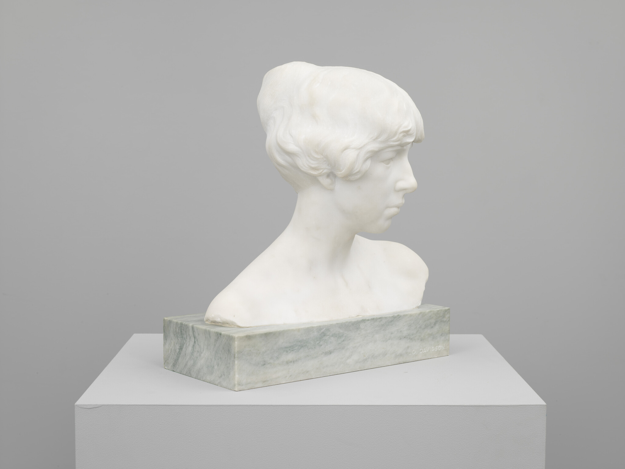 Marble bust of a young woman in profile displayed on a rectangular pedestal.