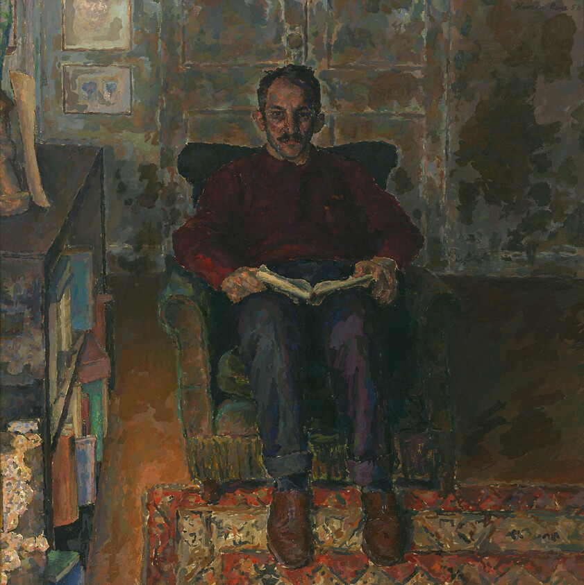 A man sits in an armchair reading a book in a dimly lit room.