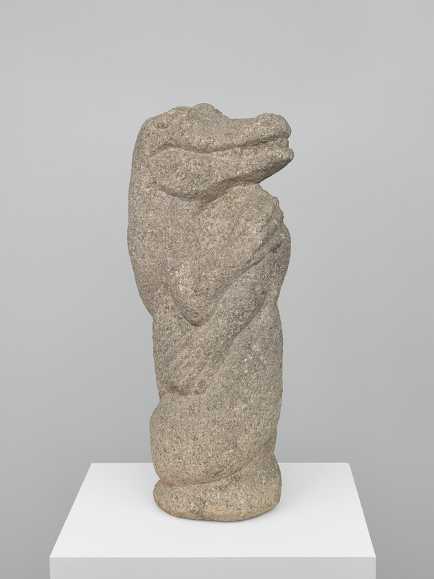 A stone sculpture of a stylized figure with its arms crossed and head tilted slightly upward, displayed on a white pedestal against a neutral background.