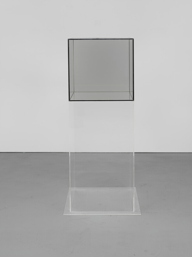 Transparent glass cube displayed on a clear acrylic pedestal in an empty white gallery.