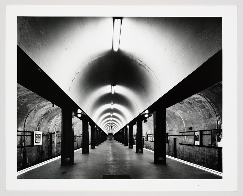 Empty underground train platform with arched ceiling and repeating lights receding into the distance.