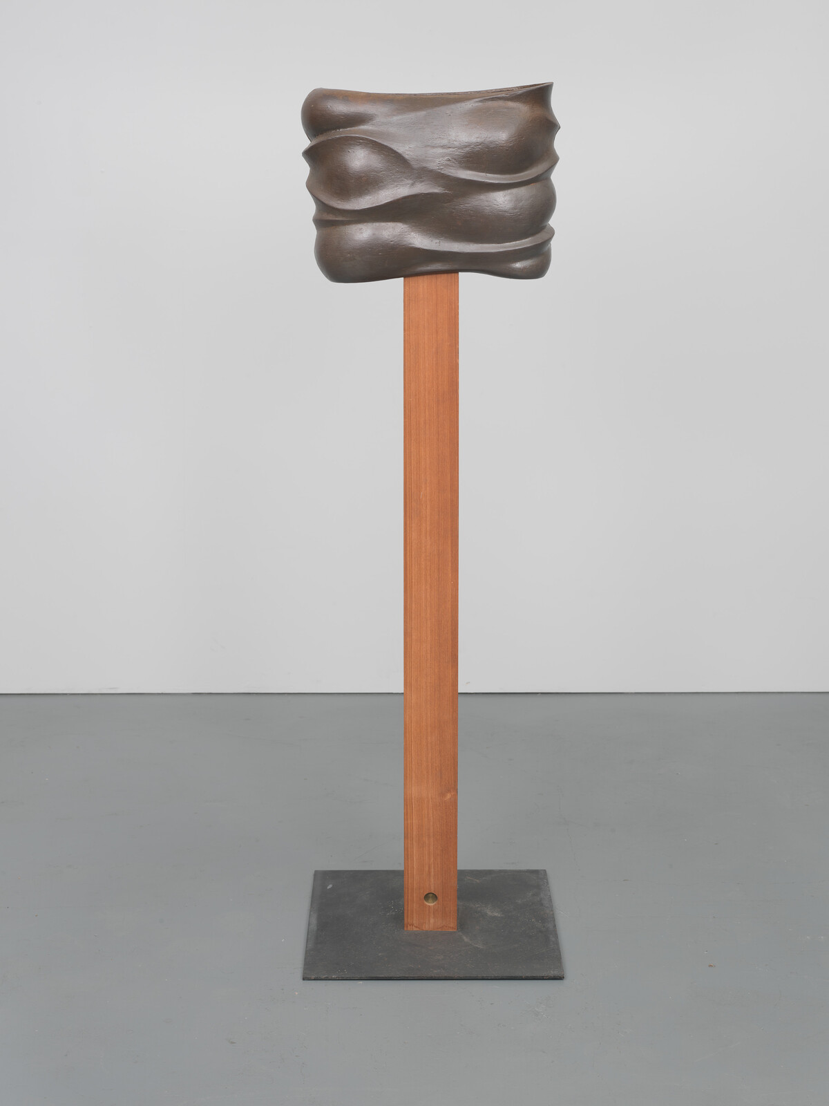A brown pole topped with a rectuangular, metallic piece full of folds and curves&nbsp;