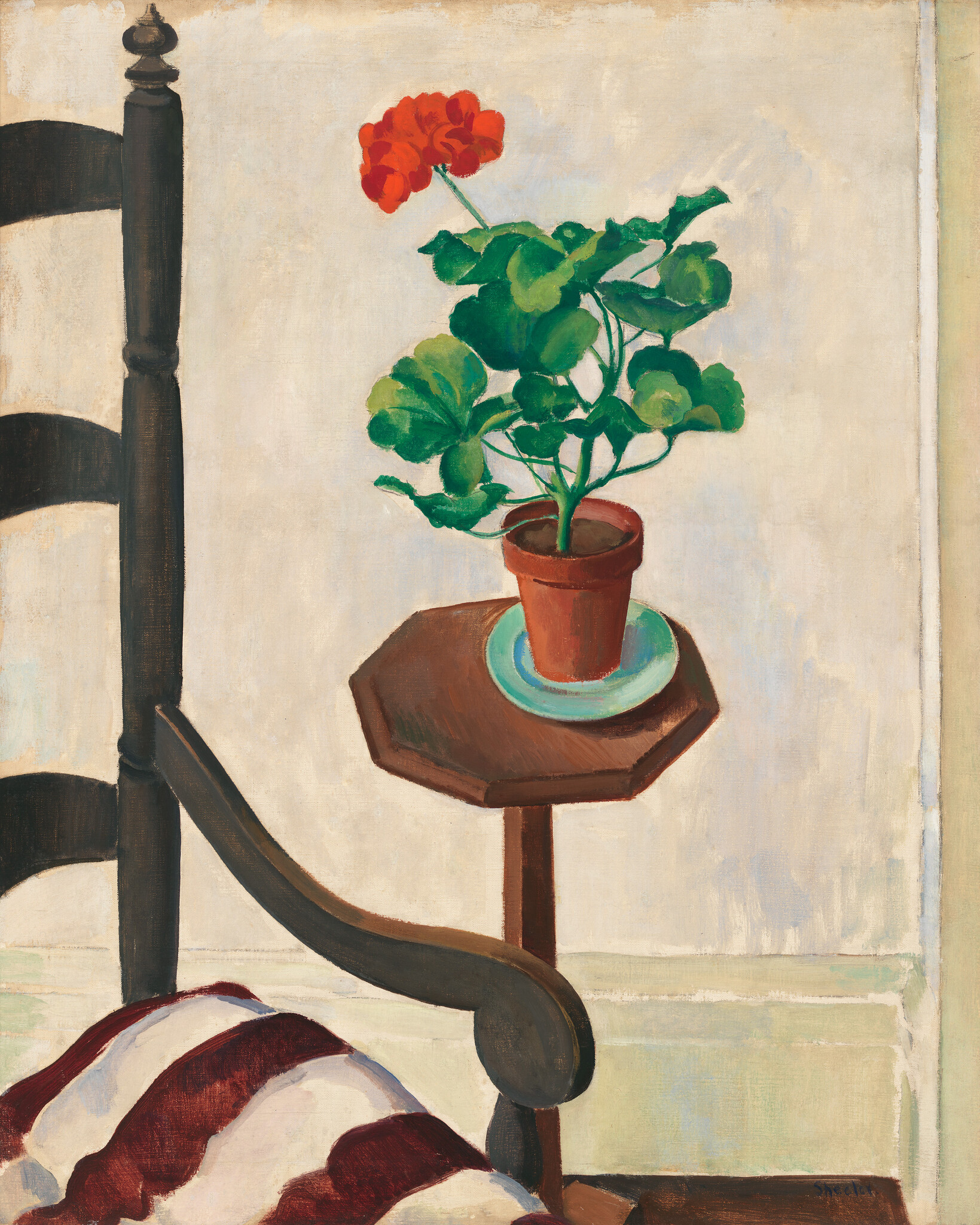 A potted red geranium sits on a small wooden side table next to a chair.