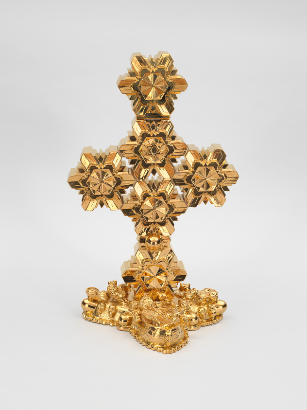 Ornate gold cross with intricate geometric patterns and a decorative base, set against a plain white background.