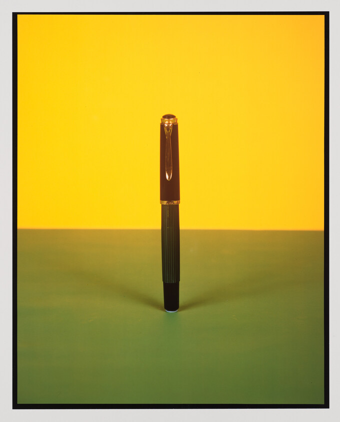 A black fountain pen stands upright on a green surface against a bright yellow background.