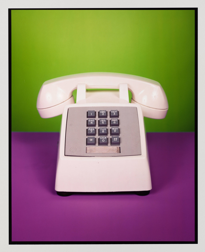 A vintage beige push-button telephone is centered against a contrasting green and purple background, framed within a black border.