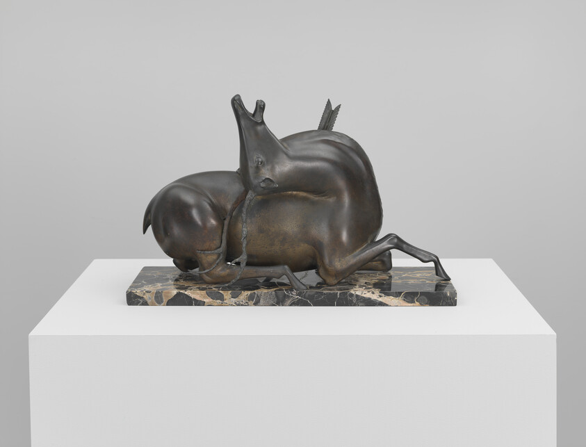 Bronze sculpture of two intertwined deer on a rectangular marble base displayed on a white plinth.