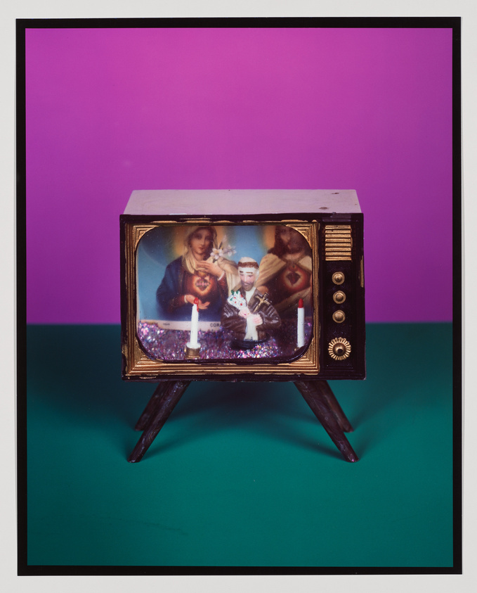 A vintage television set with a stylized image on the screen, featuring a collage of figures that resemble classical religious art juxtaposed with a modern individual, against a purple and teal background. The TV has a gold frame and stands on a simple black easel.