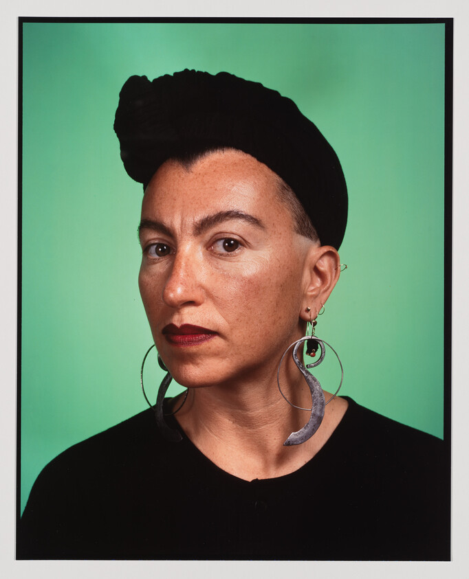 Woman with a black headscarf and large crescent-shaped earrings looking directly at the camera.