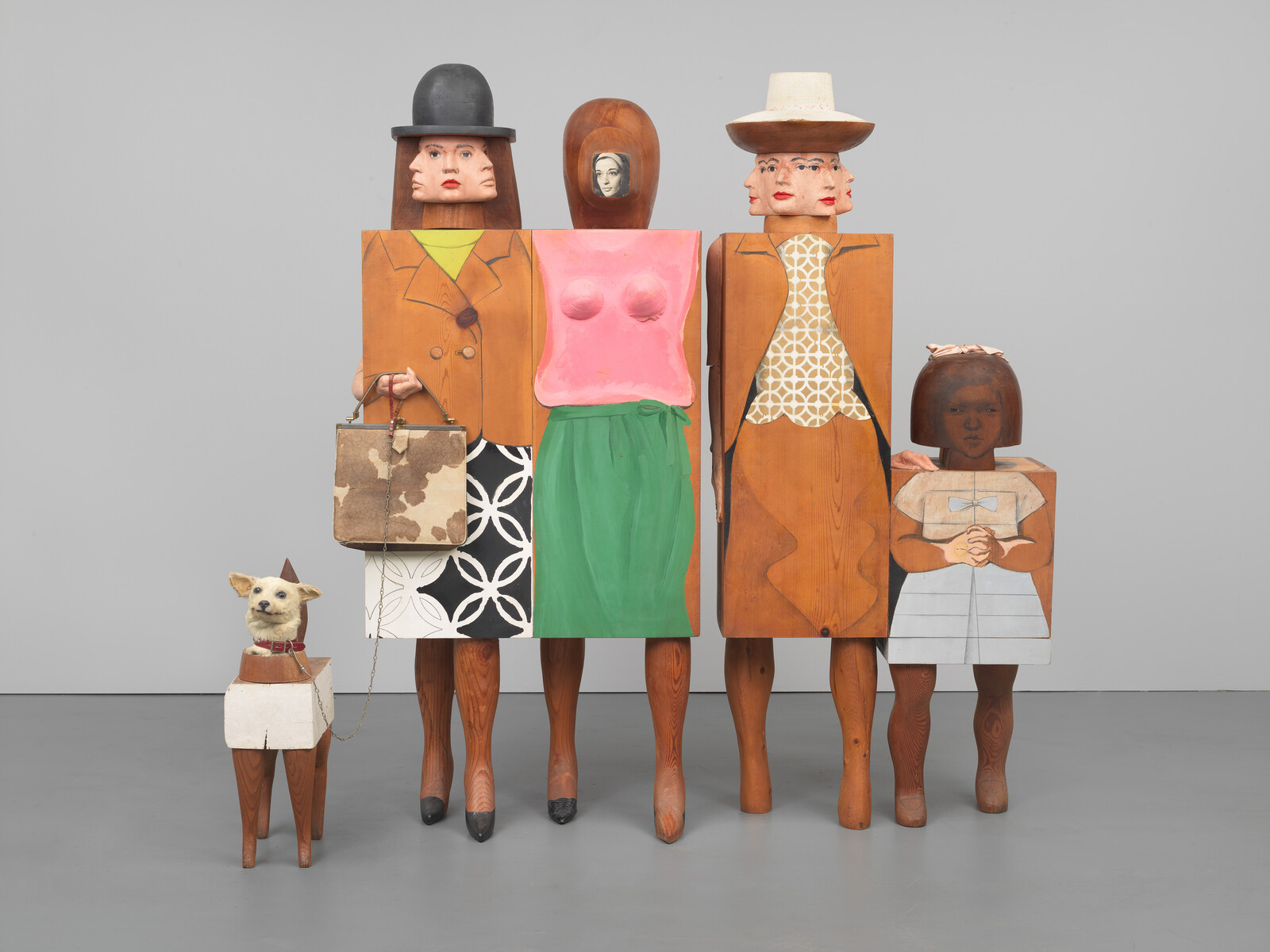 Wooden sculptures of four people and a dog, featuring multiple faces and geometric clothing designs.