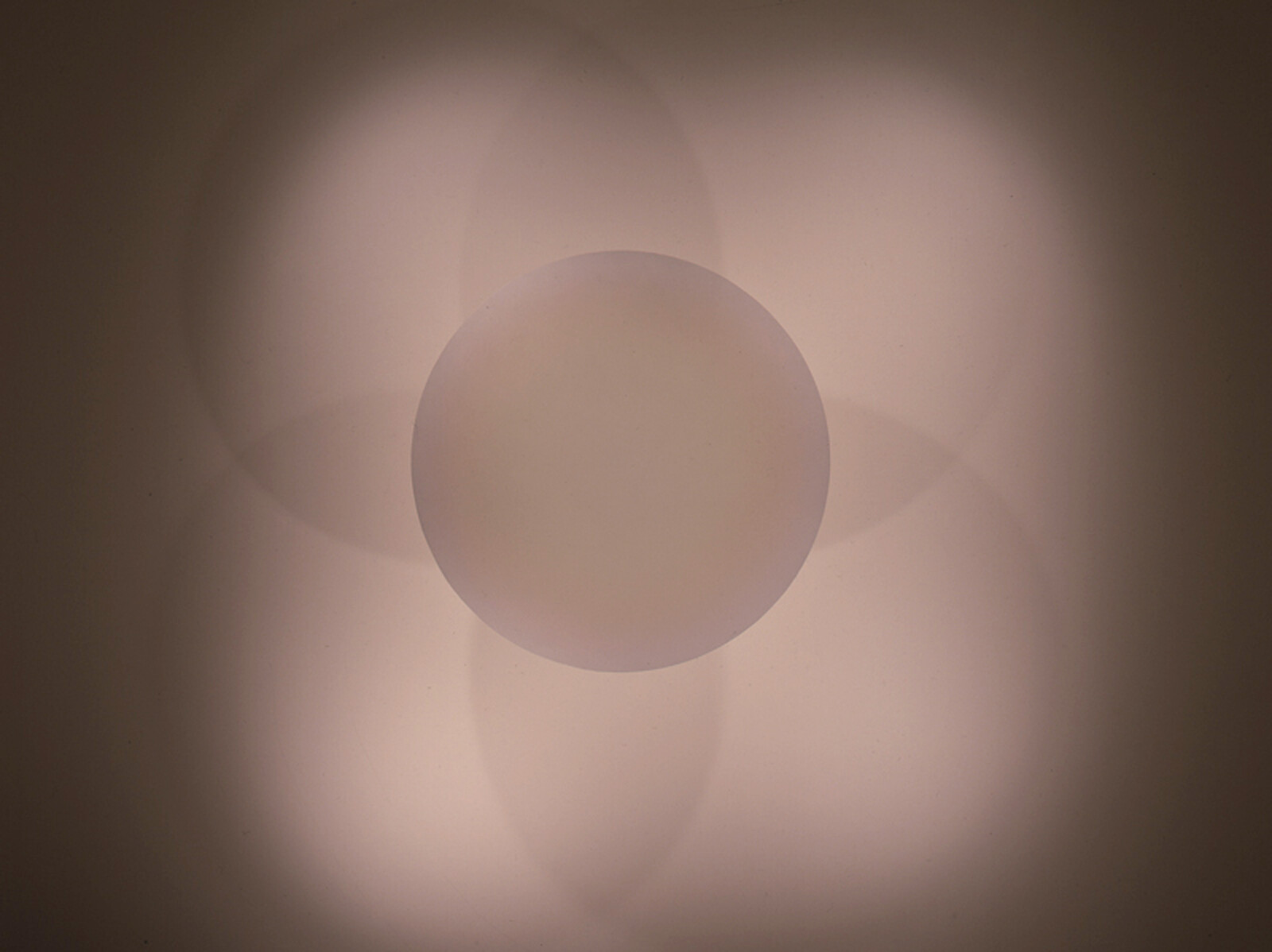 A round ceiling light casts overlapping circular shadows that form a soft flower-like pattern on the ceiling.