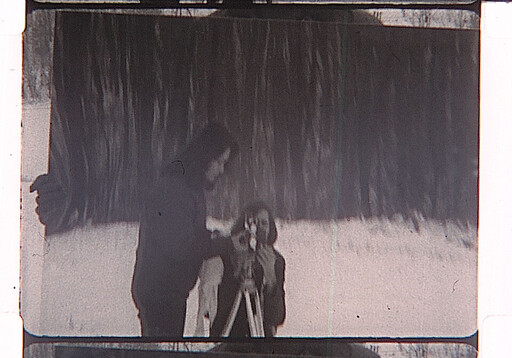 Two people set up an old camera on a tripod while standing on snowy ground.