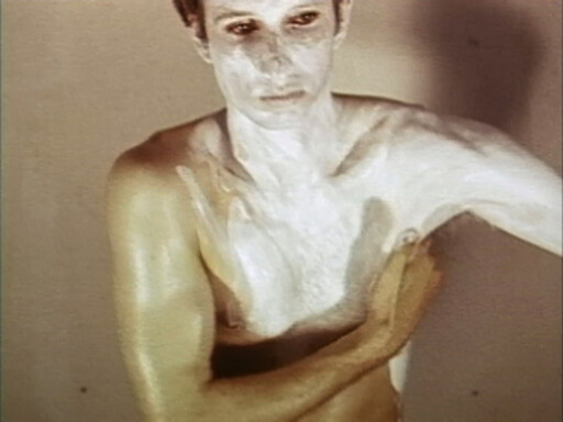 A shirtless person spreads white paint or cream across their chest and upper arm.